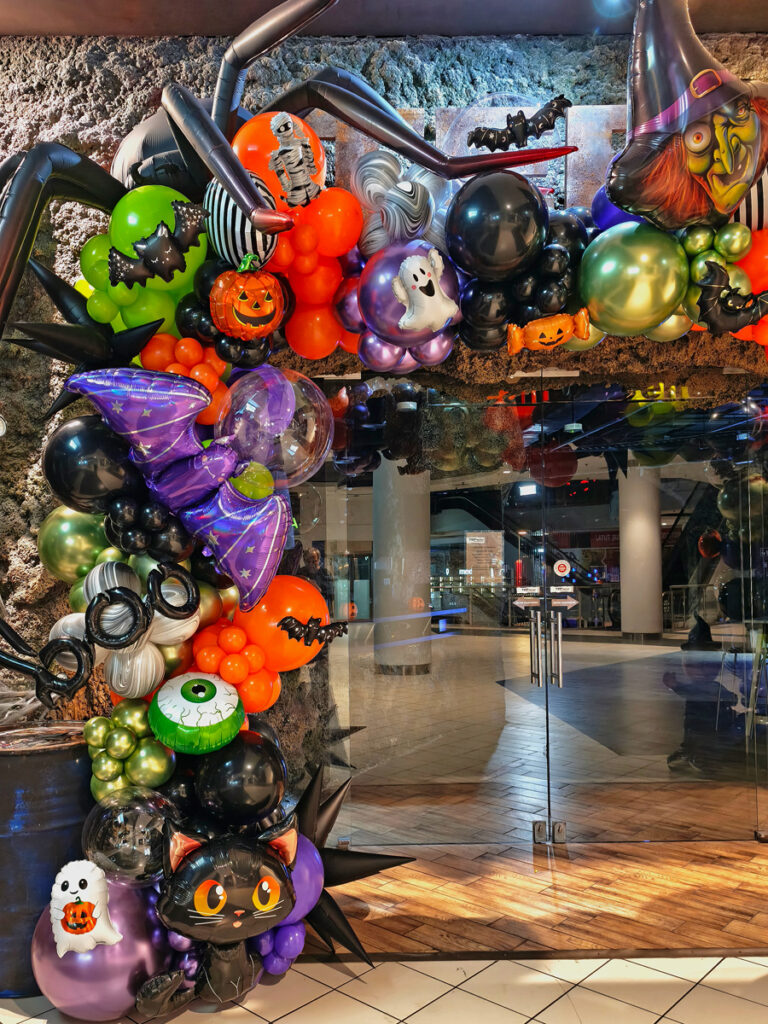 Halloweenowa girlanda balonowa w kolorach czerni, pomarańczu, zieleni i fioletu, z balonowym kotem i dyniami.