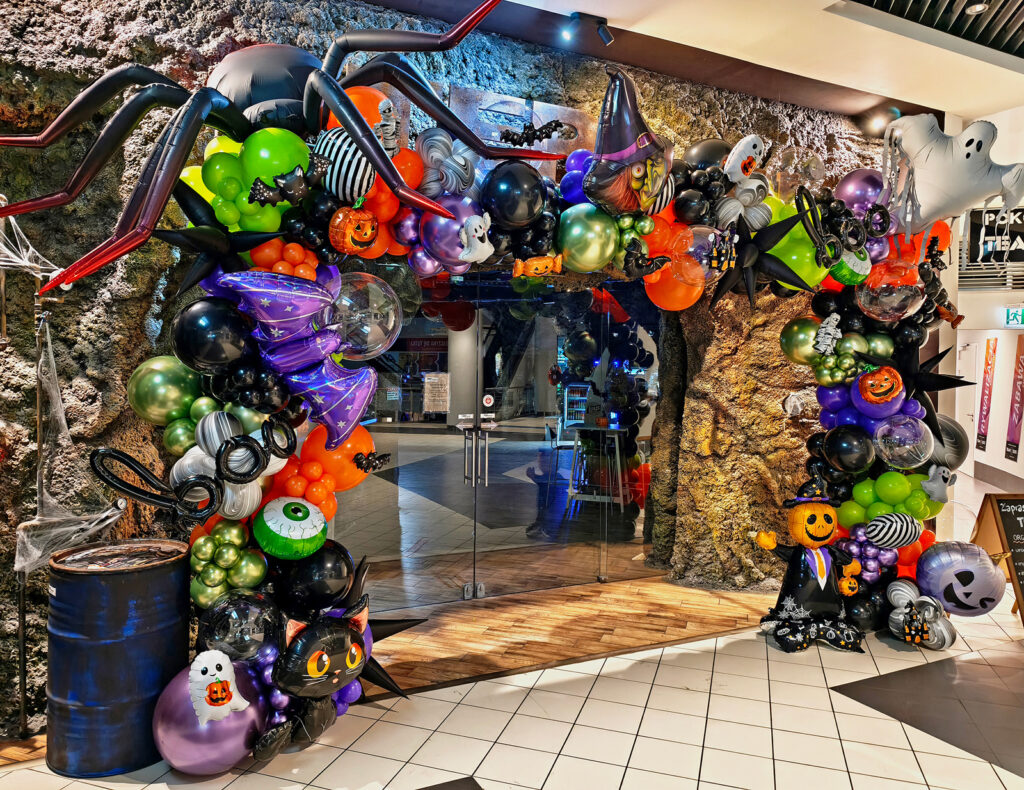 Halloweenowa scenografia balonowa przy wejściu do TEPfactor Blue City z dużym pająkiem, czarownicą, duchami i dyniami.