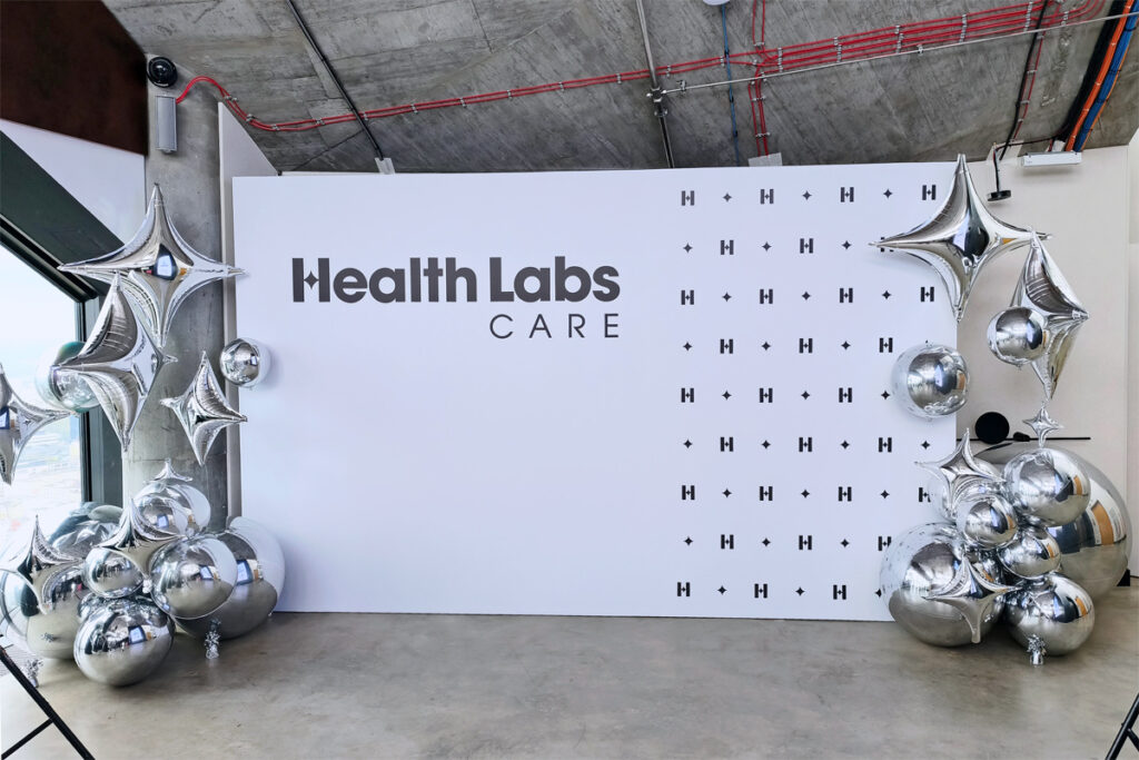 Ścianka fotograficzna Health Labs Care z dekoracjami z lustrzanych kul i srebrnych balonów w kształcie czteroramiennych gwiazd.